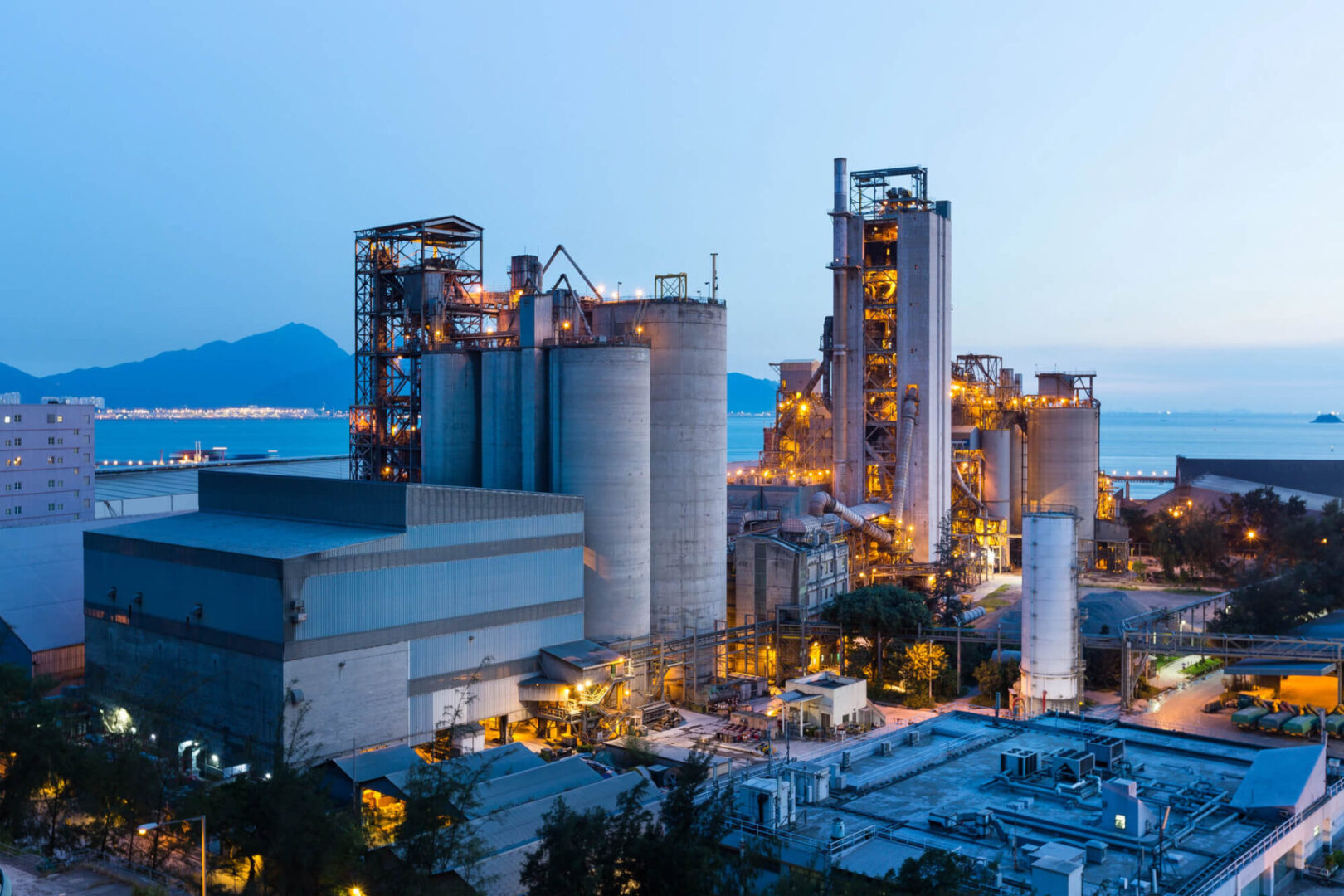 Industrial plant illuminated at dusk with mountains in the background.